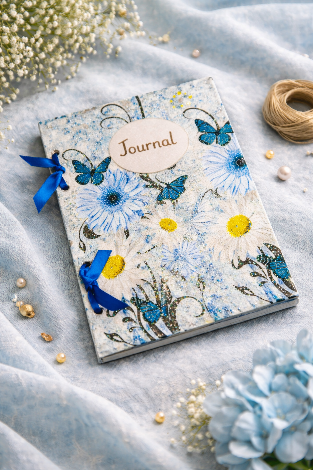 decoupage Journal with blue floral and butterfly design and blue ribbons on a wooden surface. soft fabric background