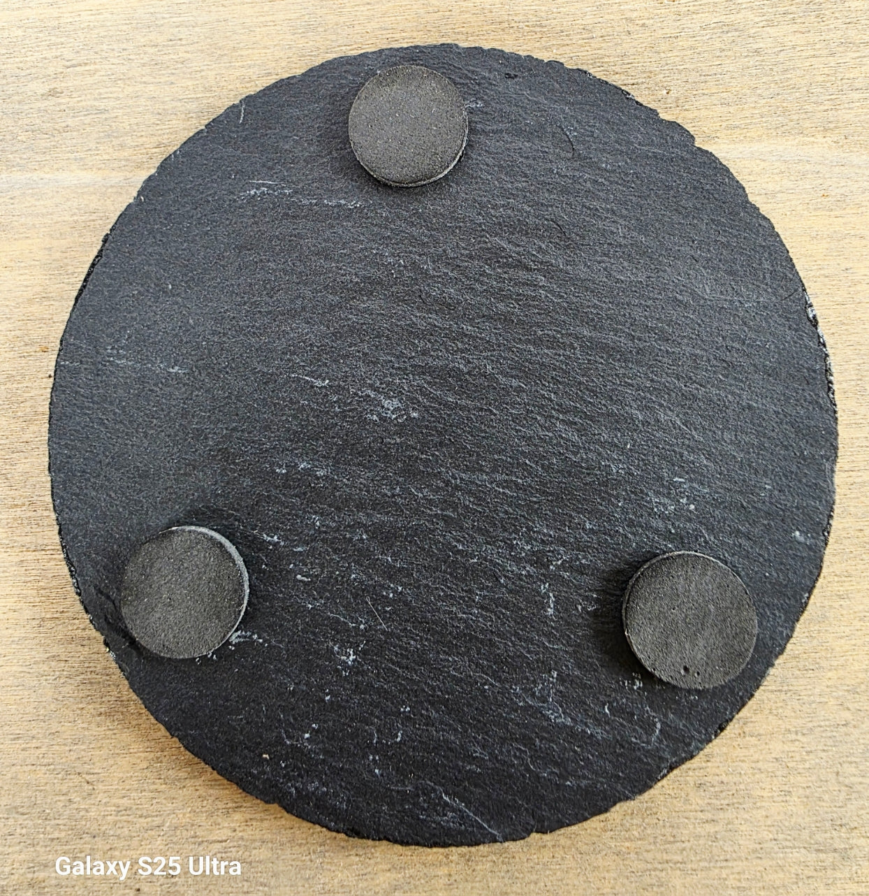 Round black slate coaster with three raised circular pads on a wooden surface