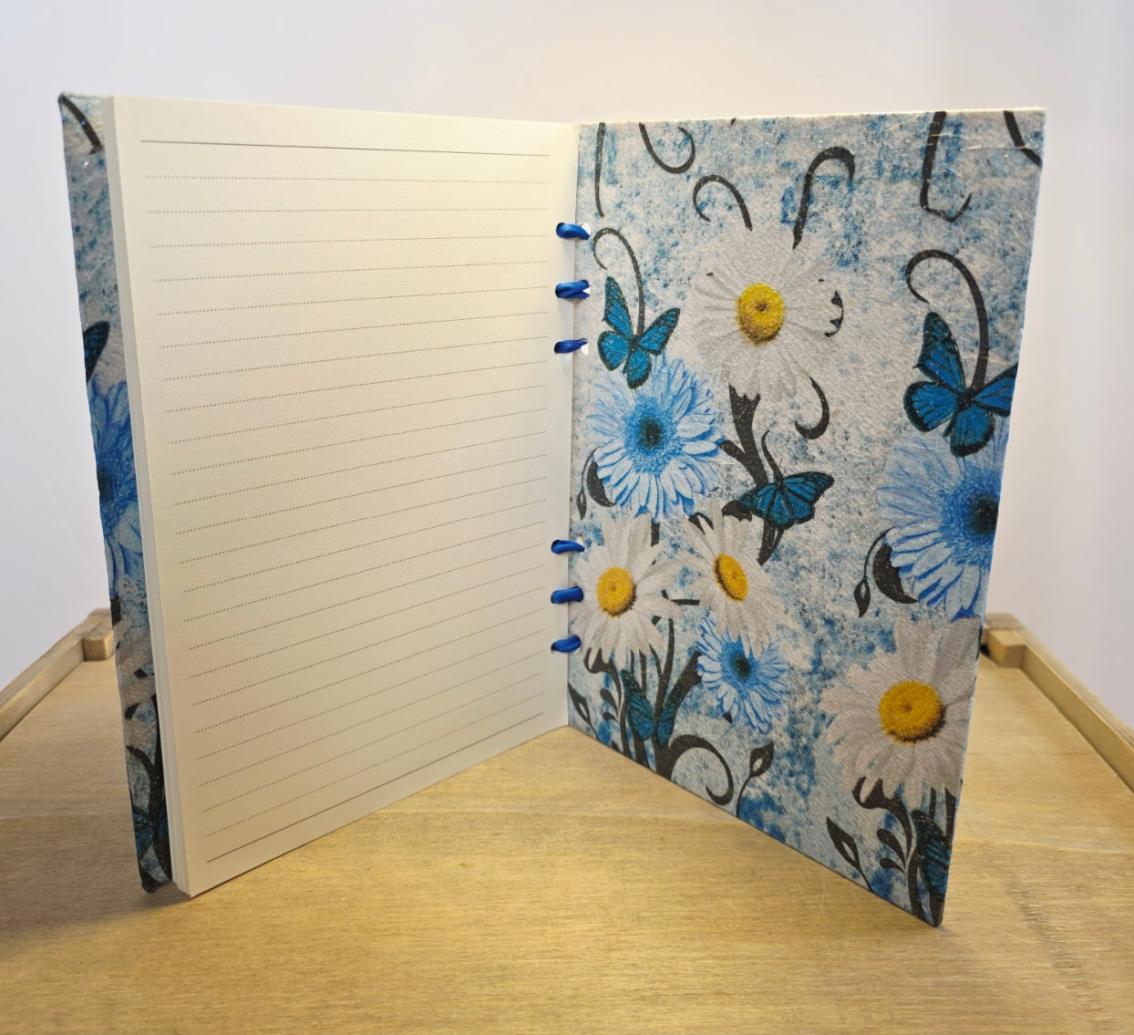 Notebook with floral and butterfly design on a wooden surface. Standing open on its edge
