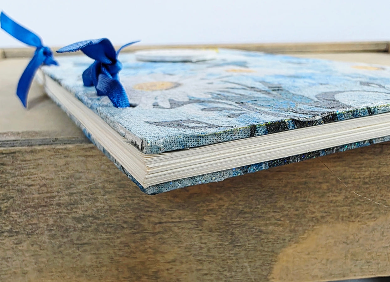 Notebook with blue floral and butterfly design on cover and lined pages. Showing side edge