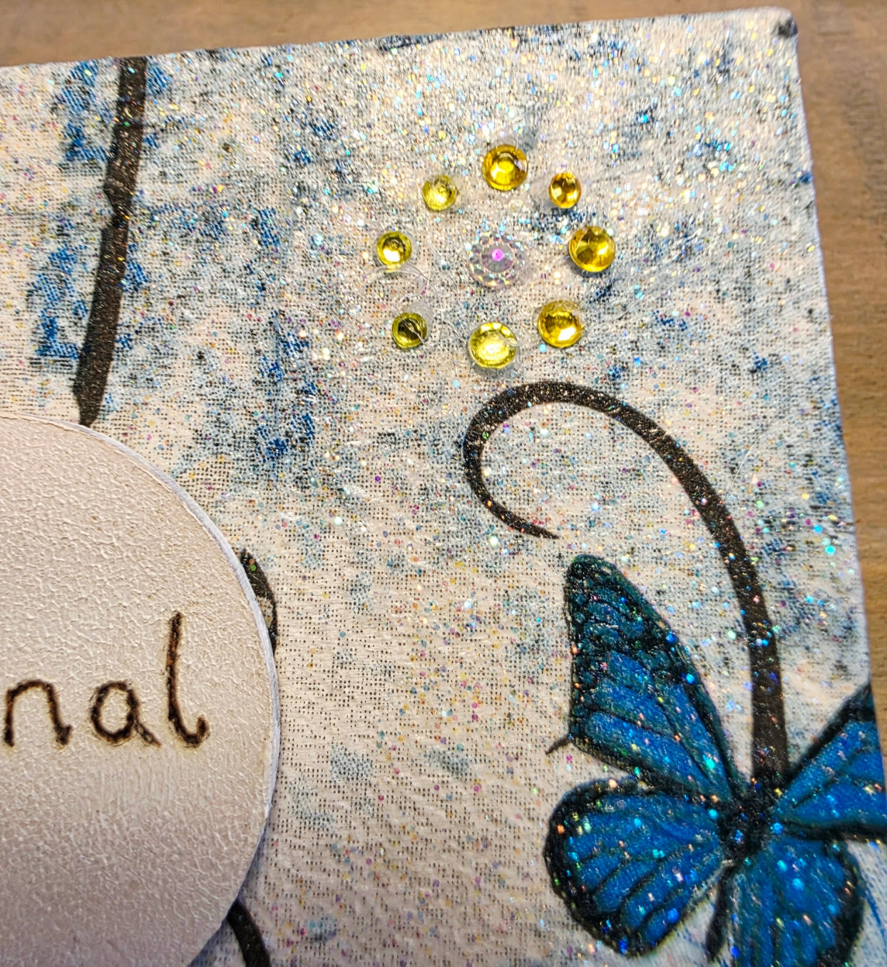 decoupage Journal with blue floral and butterfly  design and blue ribbons on a wooden surface with yellow gems