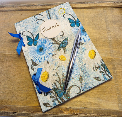 decoupage Journal with blue floral and butterfly  design and blue ribbons on a wooden surface