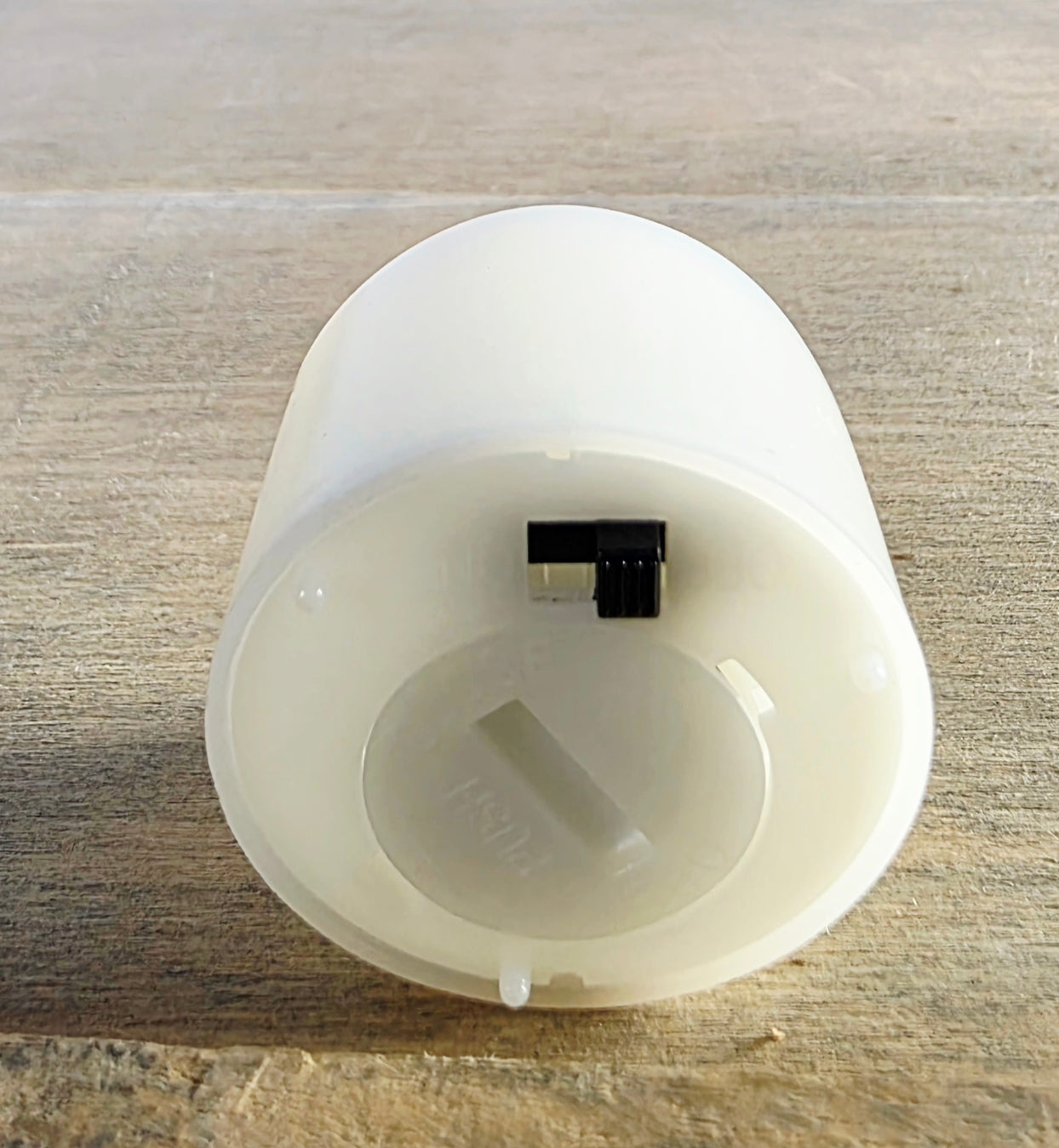 White flameless candle  with a black switch on the bottom on a wooden surface