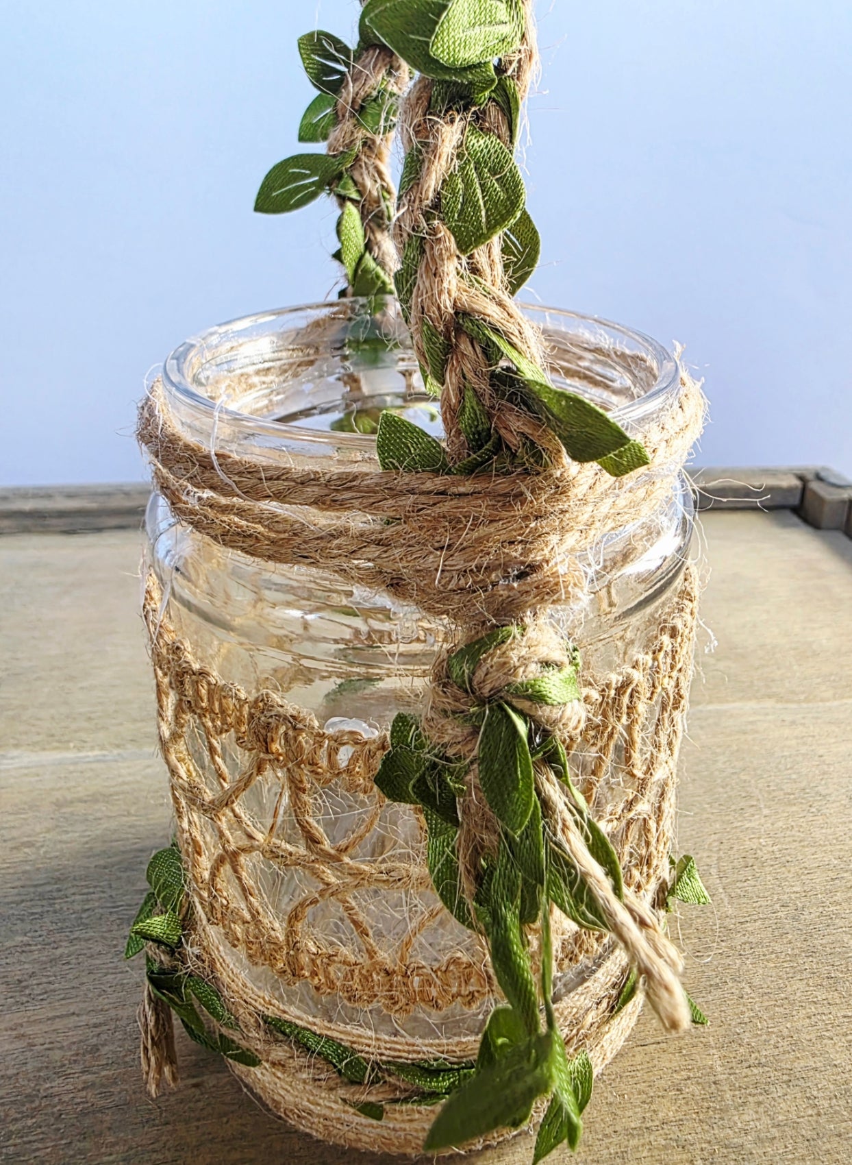 Decorative glass jar with twine and leaves handle. Burlap decor around the jar, against a light background
