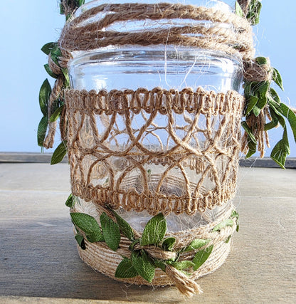 Decorative glass jar with burlap wrap and greenery on a wooden surface