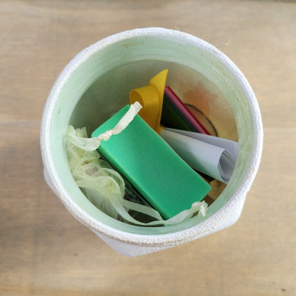 white jar with contents inside showing a green bar of soap and a yellow organza bag