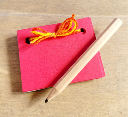 dark pink mini scrapbook tied with yellow embroidery thread. A short light brown pencil on the top