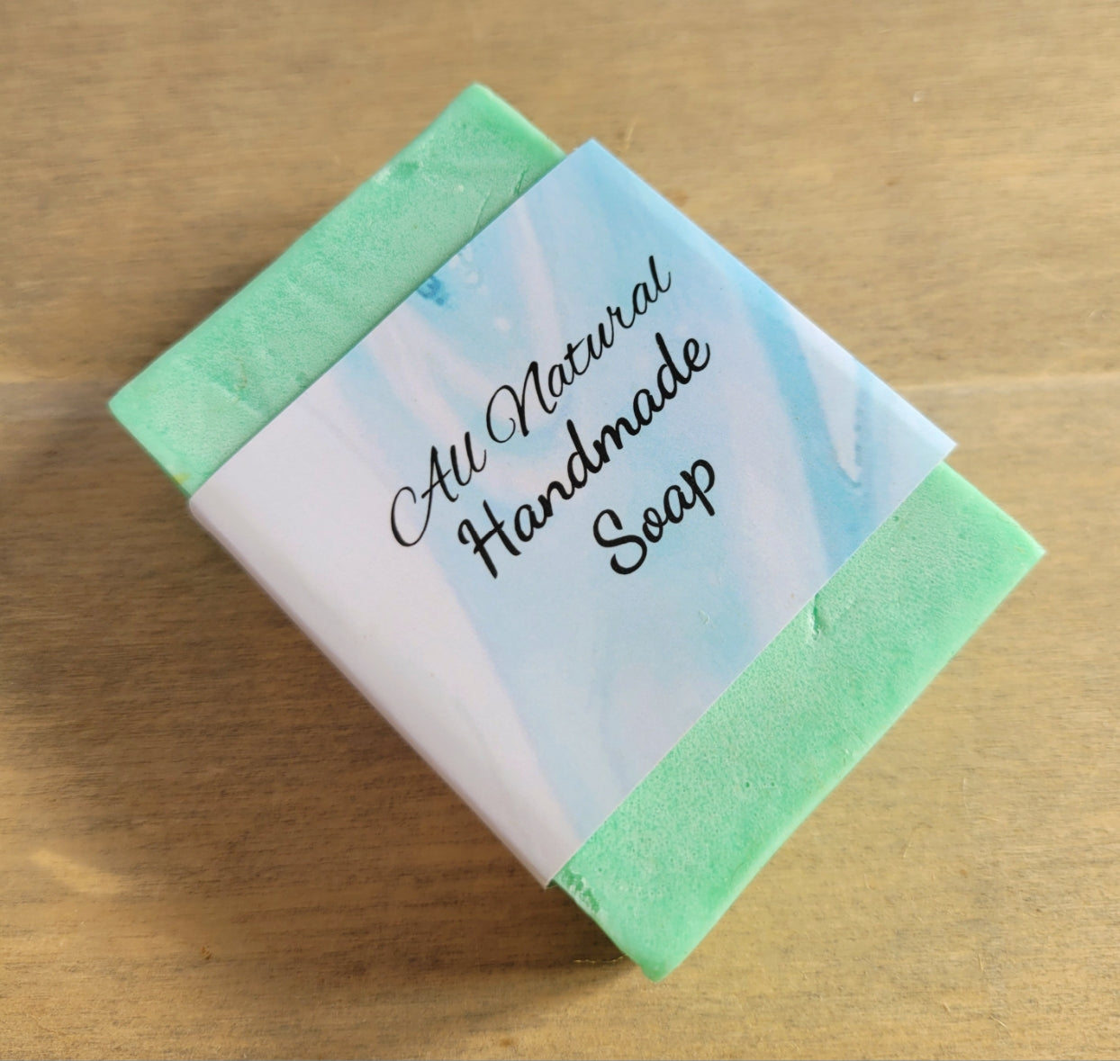 rectangular shaped light green coloured bar of soap with a blue cardboard band around it saying All natural handmade soap