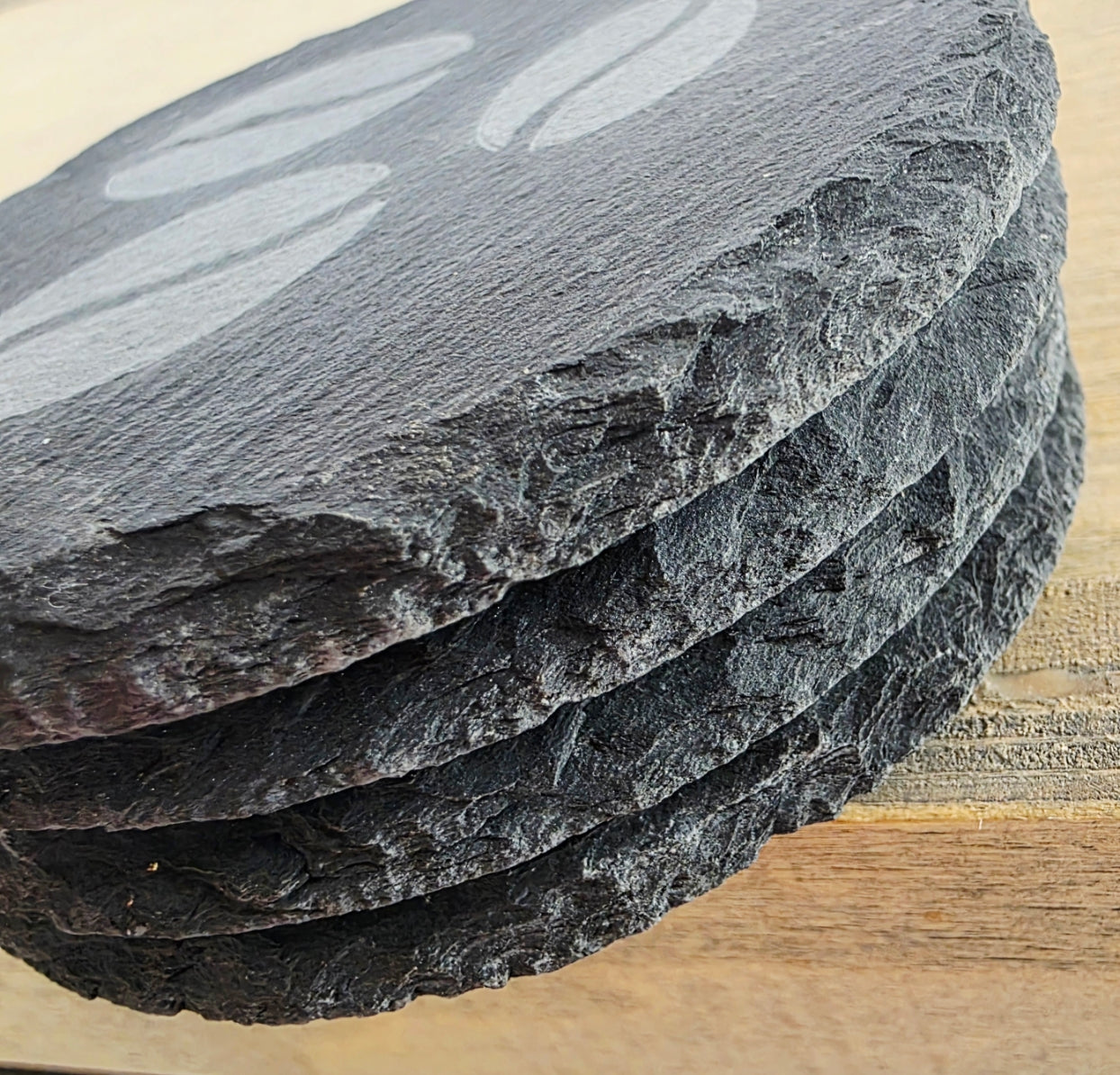 Stack of slate coasters on a wooden surface. Coffee bean design n the top