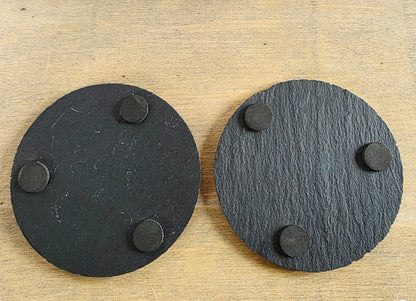 Two black circular coasters with three protective pads on the underside on each.