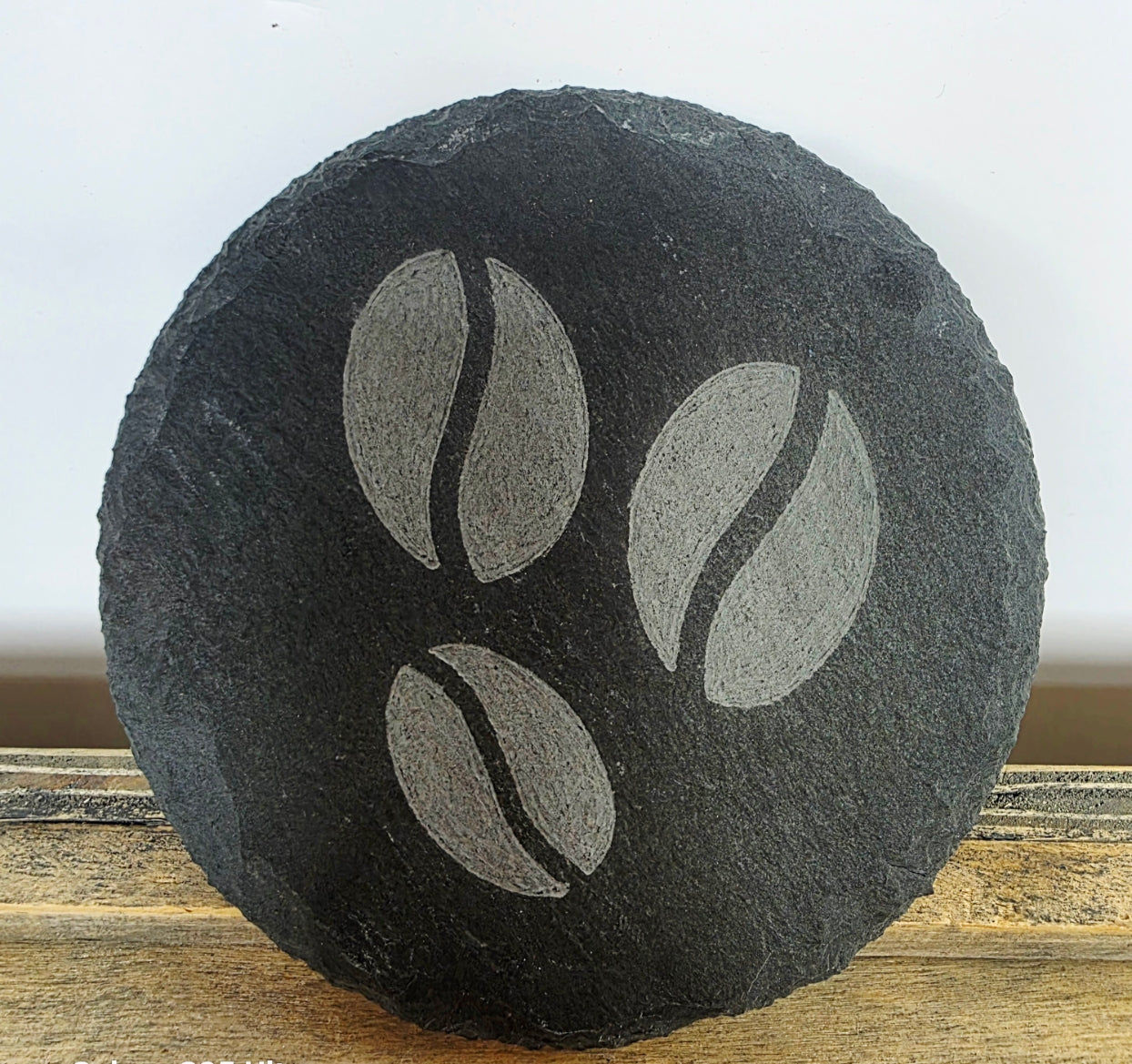 Round black slate coaster with coffee bean design on a wooden surface