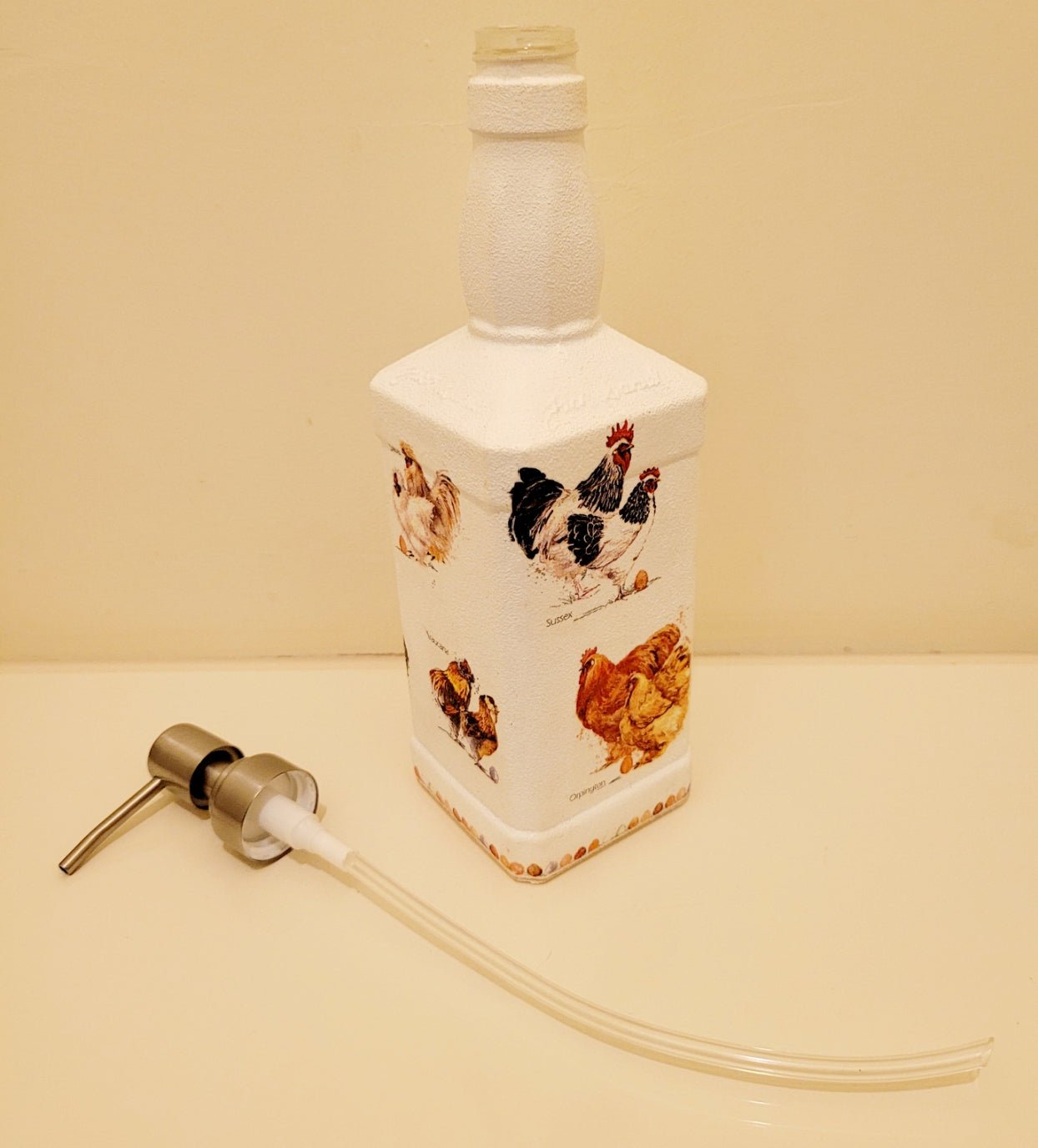 Country Inspired Soap Dispenser - white painted bottle with chickens detail around the sides. Silver pump head and tube lying next door to it