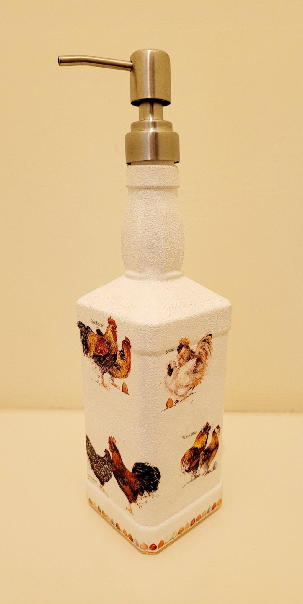 Jack daniels shaped bottle, painted white with chickens detailing around the sides, eggs around the edge at the bottom. Silver pump head