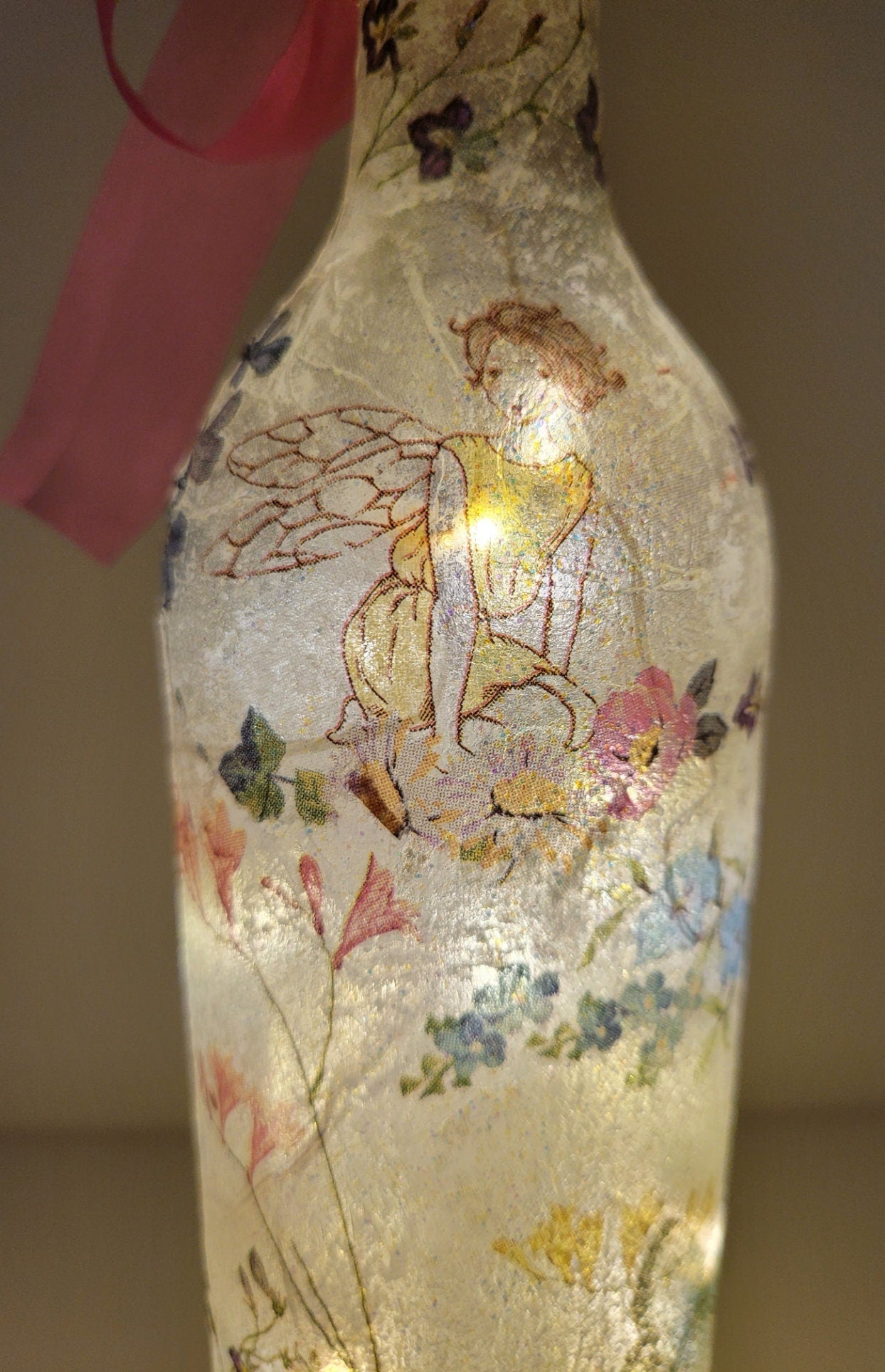 Decoupage Fairy bottle lamp - Lit up standard wine bottle with Fairy and flower butterfly detailing. Pink organza ribbon tied around the neck of the bottle. Cork LED lights