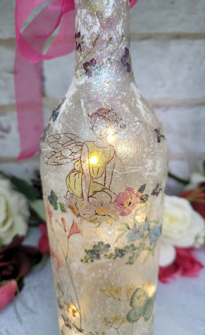 Decoupage Fairy bottle lamp - Lit up standard wine bottle with Fairy and flower butterfly detailing. Pink organza ribbon tied around the neck of the bottle. Cork LED lights
