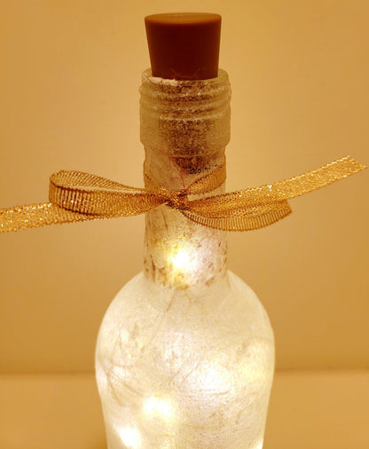 Lit up wine bottle with gold ribbon tied around the neck. Brown plastic cork