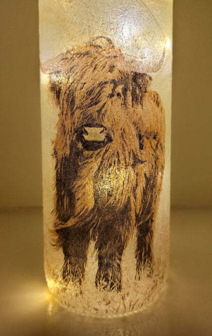Lit up standard shape wine bottle with highland cow detailing on the front near the bottom. Cork LED lights