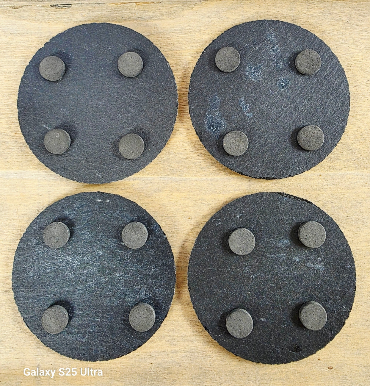 Four round, black slate coasters with four protective pads on each one on their undersides