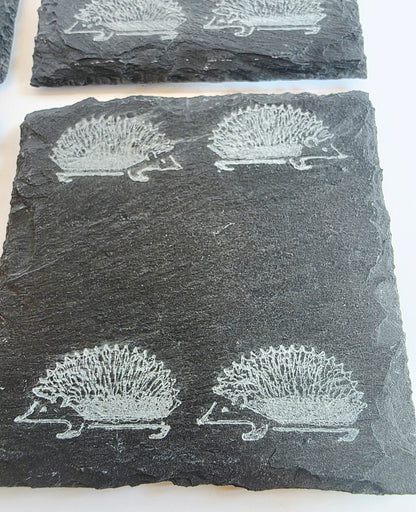 Dark grey slate coasters featuring engraved hedgehog designs, arranged on a white surface.