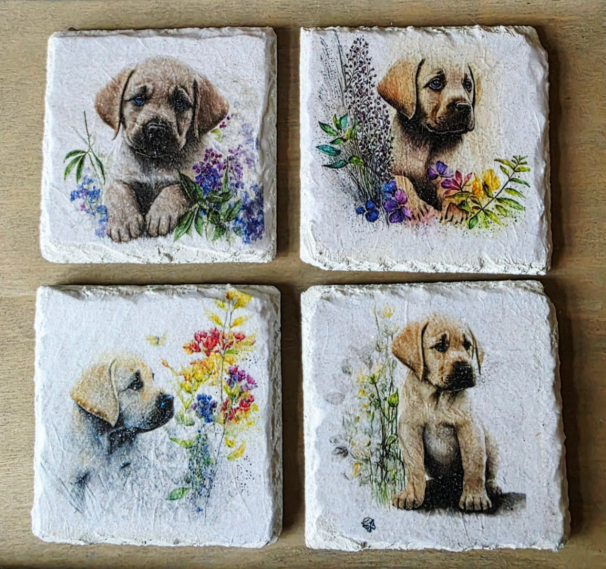 Four square slate tiles with illustrations of puppies and flowers on a wooden surface.