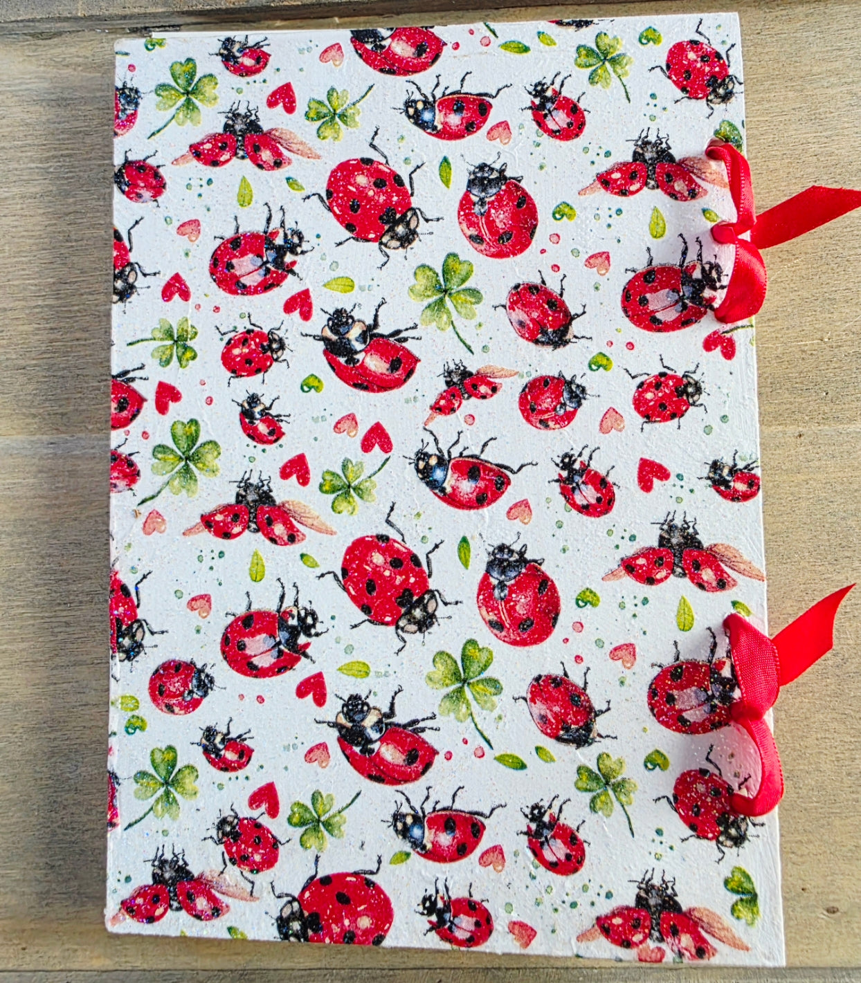 notebook with ladybug pattern on a wooden surface. bound with red ribbon