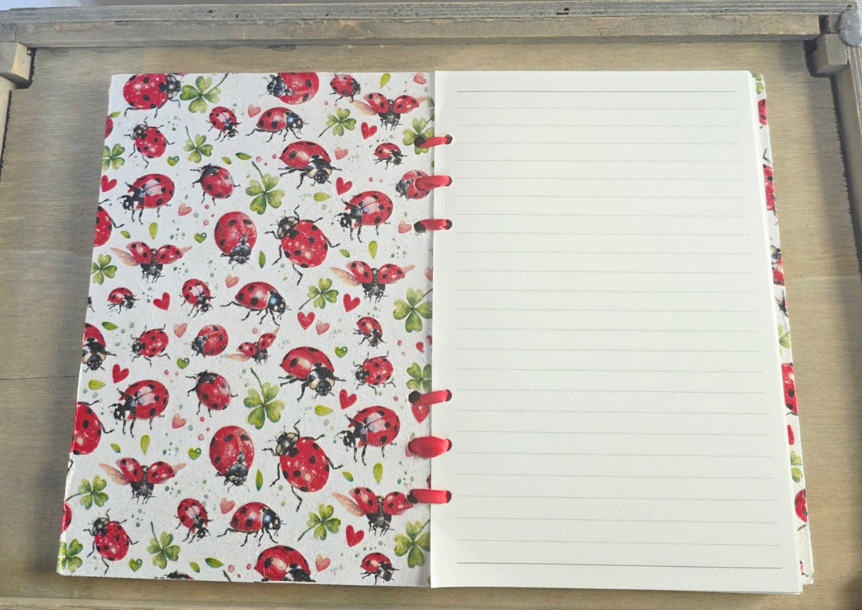Notebook with ladybug pattern on the cover and lined pages. red ribbon bound