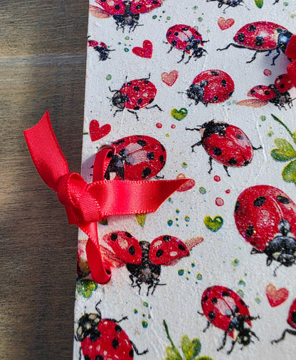 Notebook with ladybug and heart pattern and a red ribbon on a wooden surface