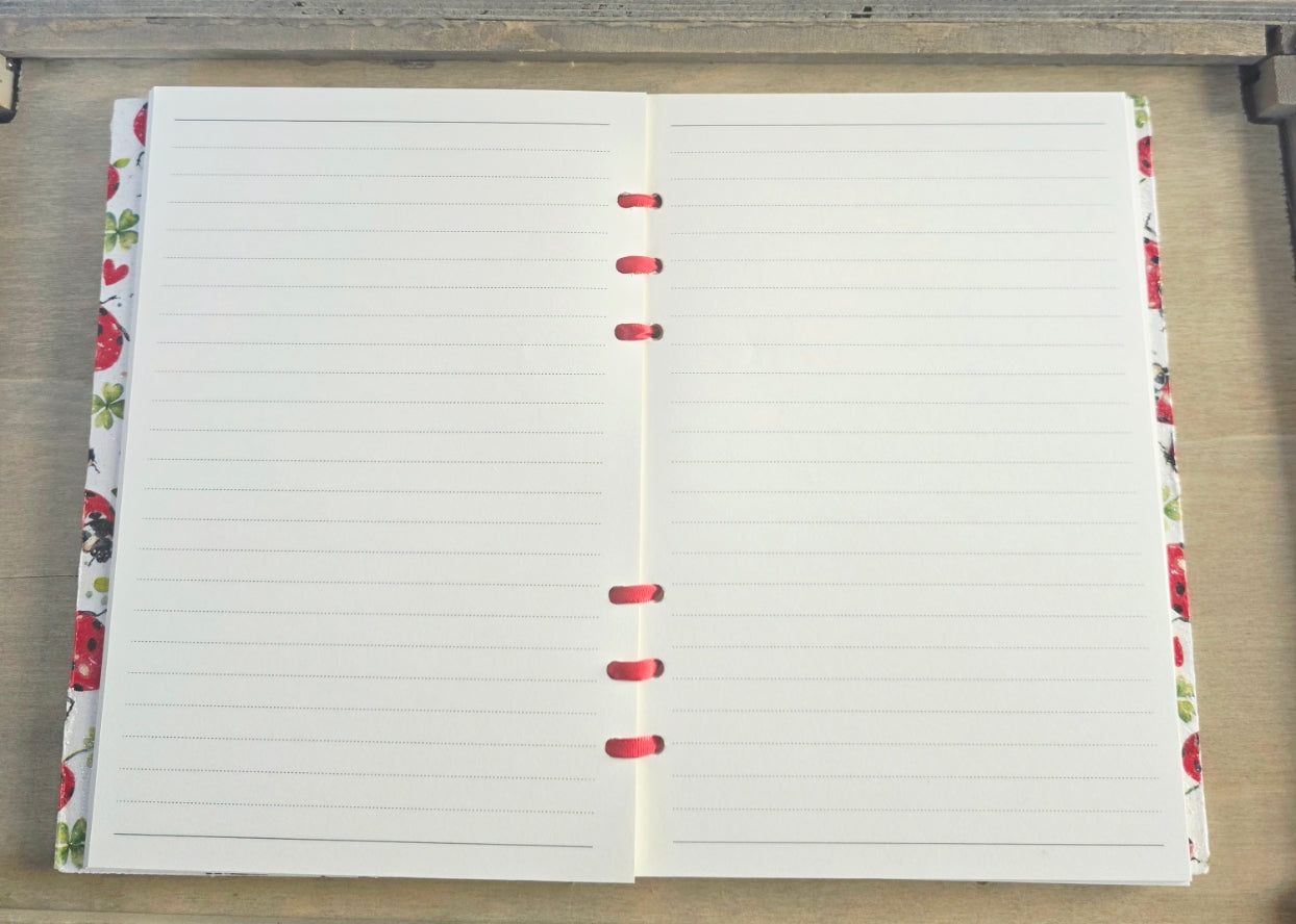 Open notebook with lined pages on a wooden surface. red and white cupboard and red ribbon bound.