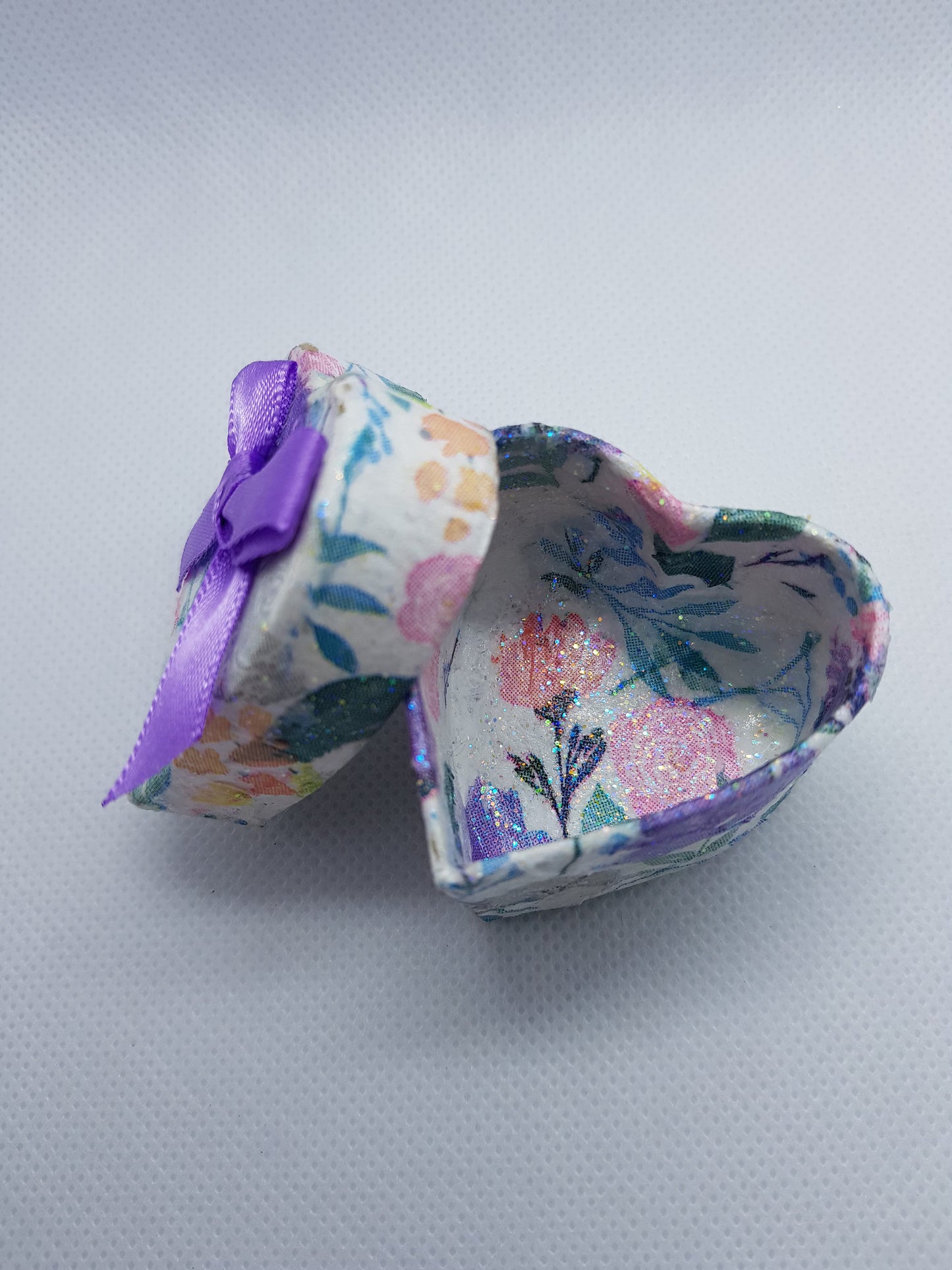 Heart-shaped jewelry box with floral design and purple ribbon on a light gray background