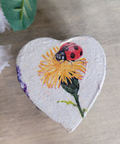 Heart-shaped decorative item with a ladybug and flower design on a wooden surface