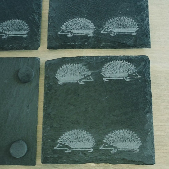 Video of four square slate coasters with an engraved pattern of four hedgehogs on each coaster