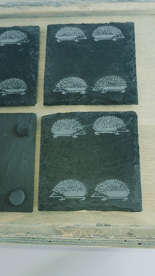 Video of four square slate coasters with an engraved pattern of four hedgehogs on each coaster