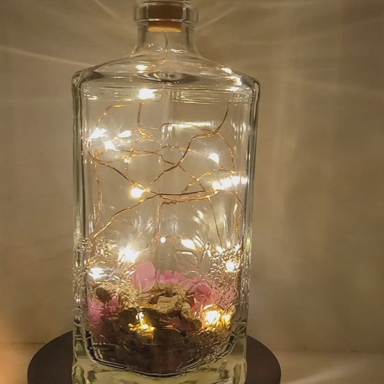 Rotating example of a Lit up hexagonal bottle with pink and gold coloured stones inside. Cork LED lights