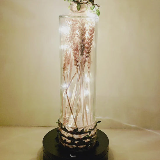 A wheat filled bottle with jute twine and leaves, LED lights, rotating on a stand