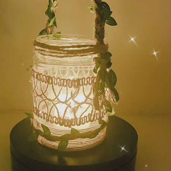 Video of a rotating Decorative lantern with decorative burlap design. Jute handle with leaves glowing light on a table in a cozy living room setting.
