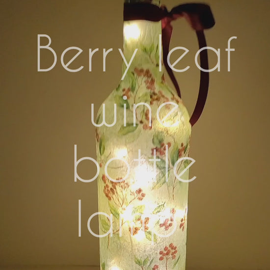 A rotating example of a Lit up wine bottle with green leaf and red berry detail. Cork LED lights and red ribbon embellishment.