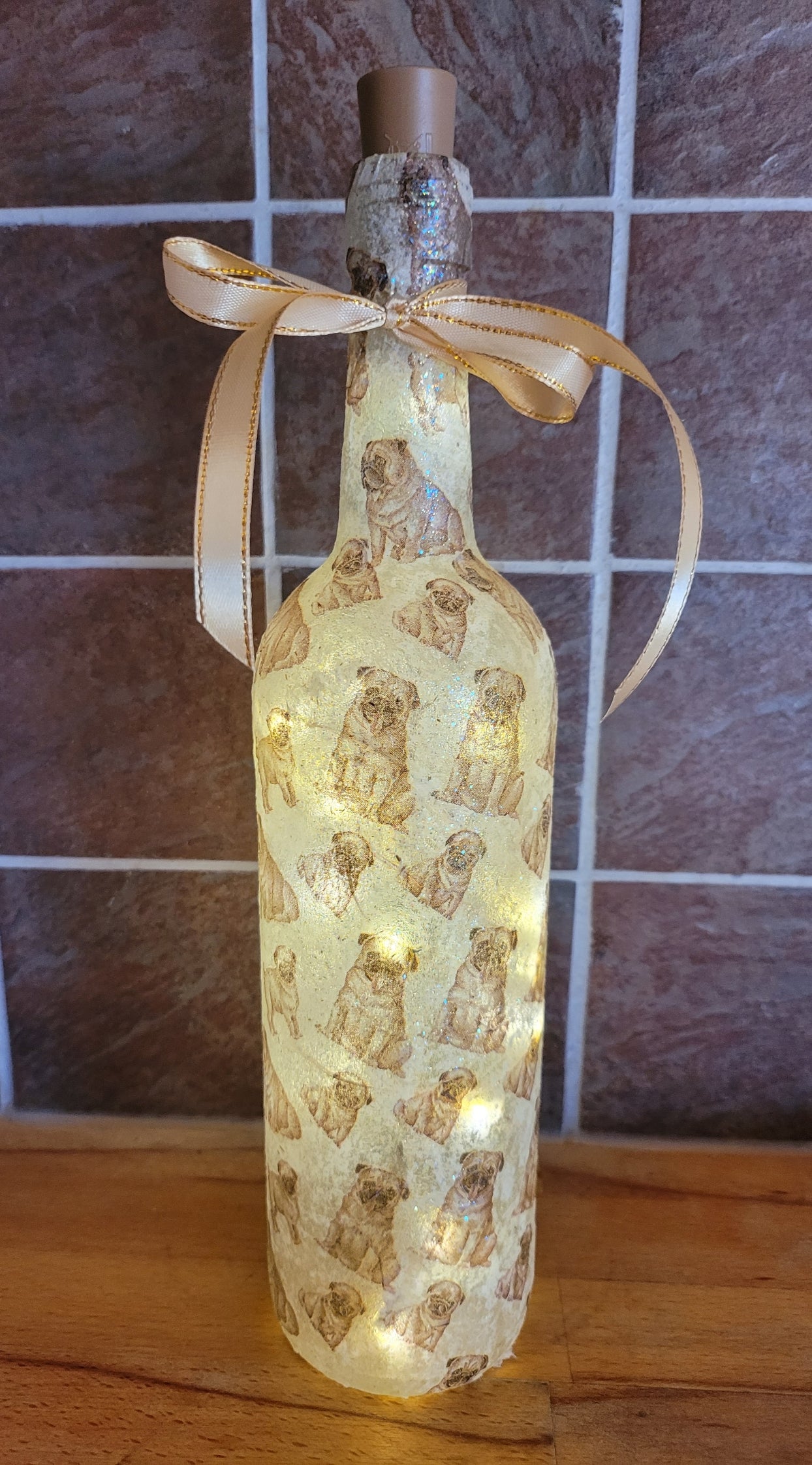 wine bottle decorated with tiny pug dog images. Cork LED lights and gold ribbon embellishment