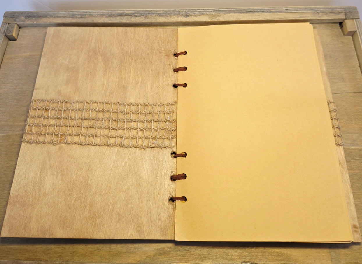 Open notebook with wooden cover on a wooden surface. Burlap mesh decoration on the inside front cover. Brown plain pages