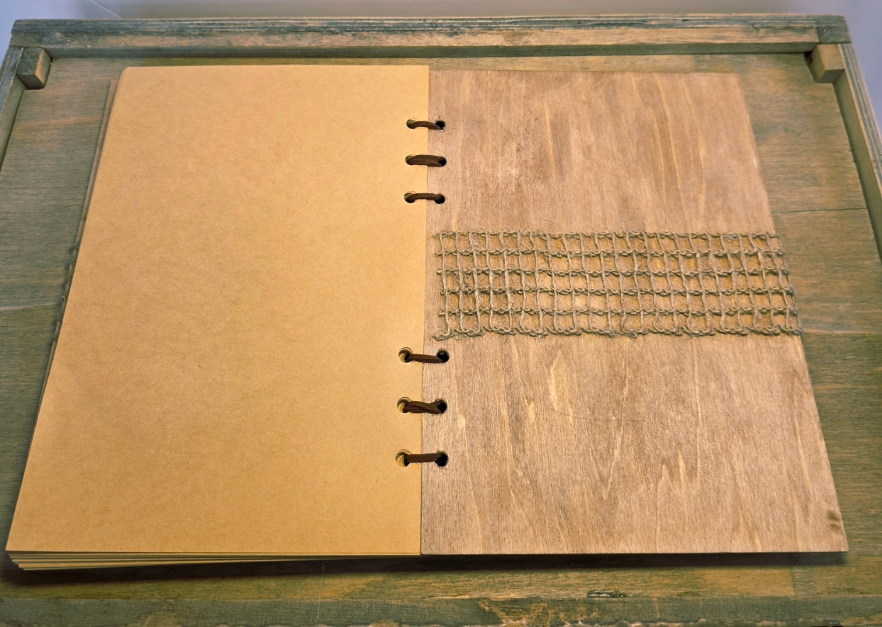 Open notebook with wooden cover on a wooden surface. Burlap mesh decoration on the inside back cover. Brown plain pages