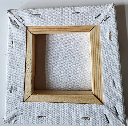 back of a piece of stretched white canvas showing the wood frame and staples