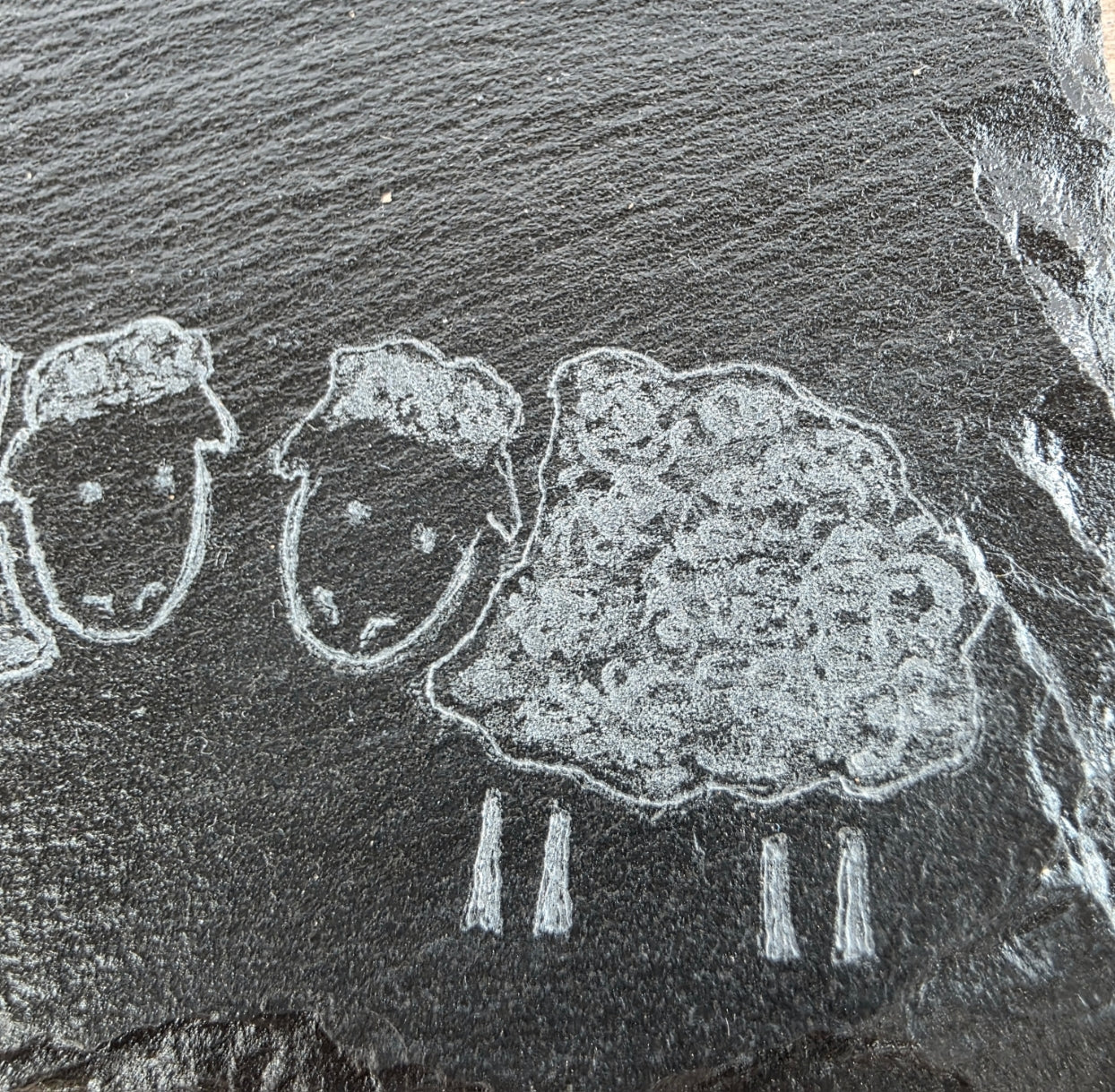 Rock engraving of three sheep on a dark stone slate tile