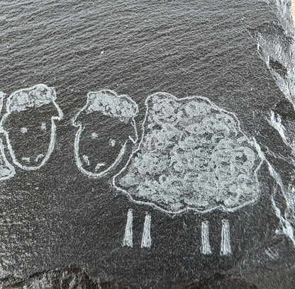 Rock engraving of three sheep on a dark stone slate tile