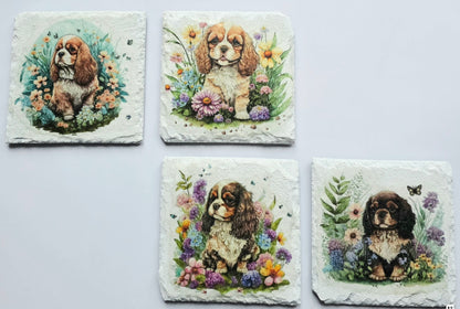 Four White slate coasters with four different paintings of a king charles spaniel puppy surrounded by flowers on a white background