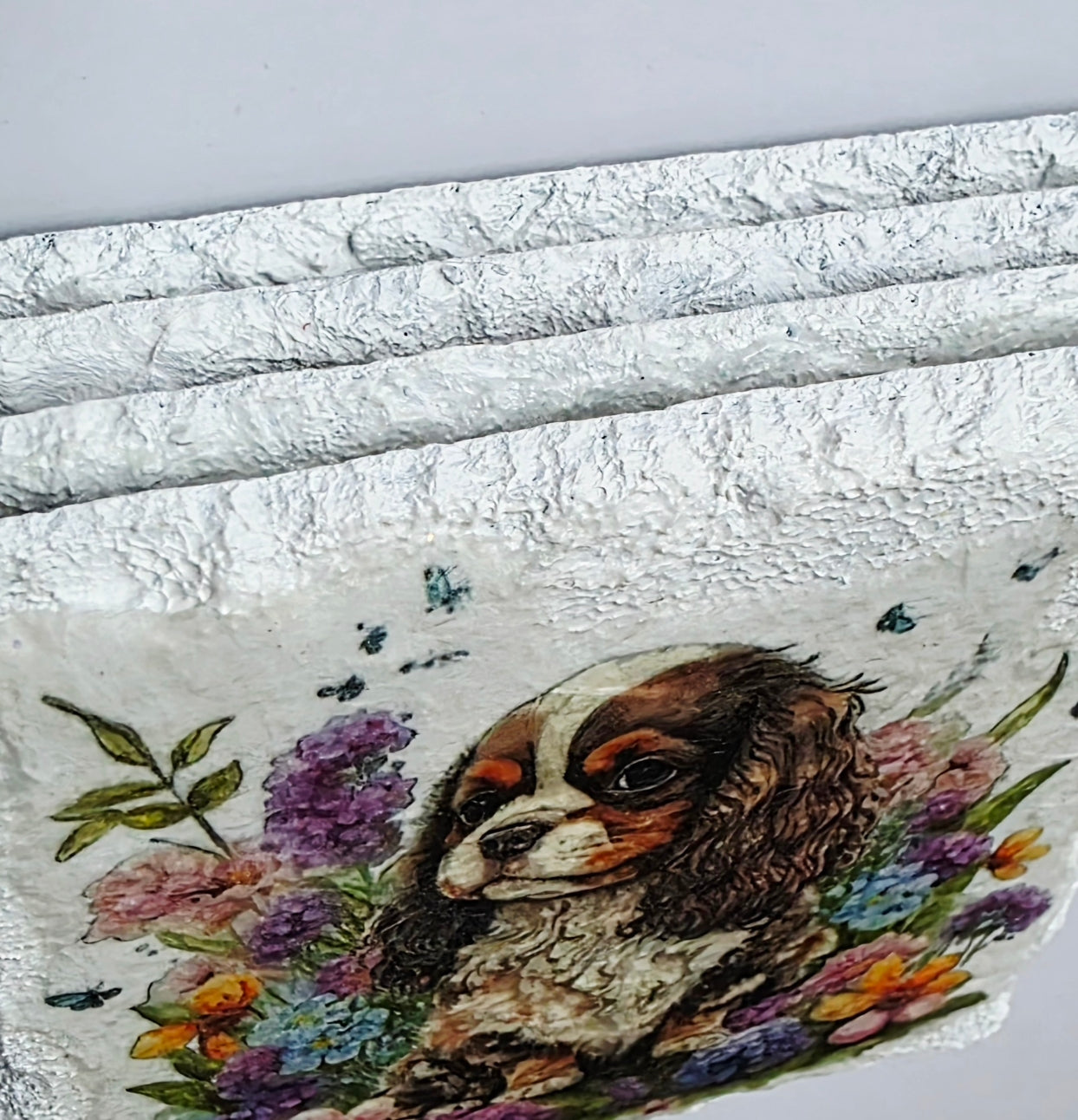 Four white slate coaster edges with a spaniel dog and floral design on a white background