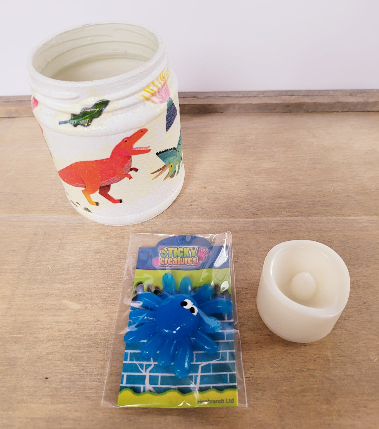 white painted jar with Dinosaur detail. A sticky blue monster toy and cream flameless plastic candle
