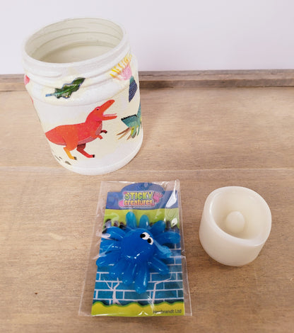 white painted jar with Dinosaur detail. A sticky blue monster toy and cream flameless plastic candle