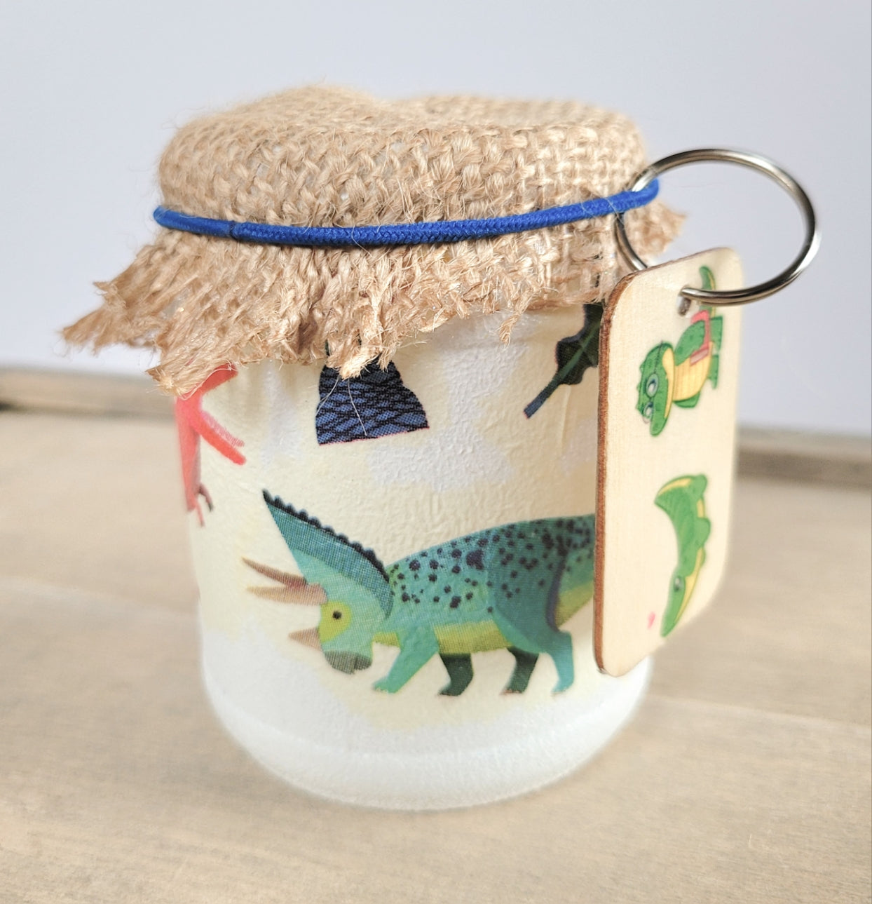 white painted jar with Dinosaur detail, wooden keyring with green Dinosaur on it, brown hessian lid secured with a blue elastic band