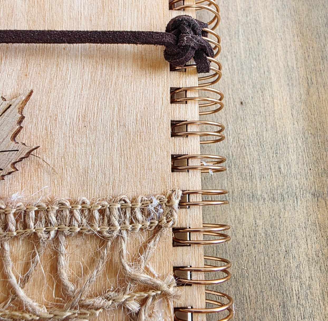 Close-up of a wooden notebook with a textured cover and metal spiral binding. faux suede tie
