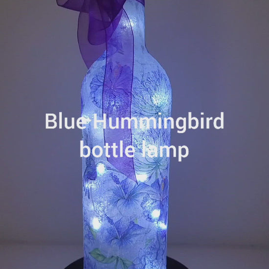 Rotating Lit up bottle with blue Hummingbird and blue flowers  detail. Cork lights. Purple ribbon